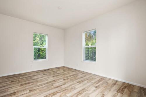 An empty room with wood floors and windows.