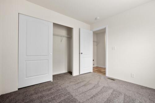 An empty room with white closet doors and carpet.