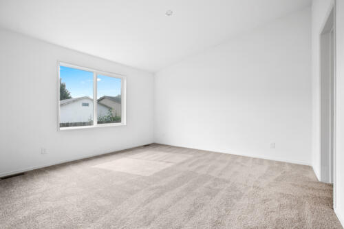 An empty room with white walls and tan carpet.