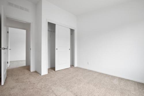 An empty room with tan carpet and white closets.