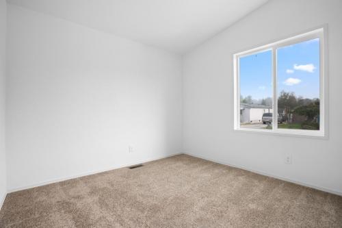 An empty room with a window and tan carpet.