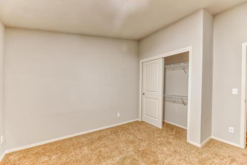 An empty room with tan carpet and a closet.