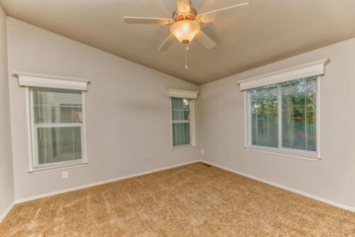 An empty room with a ceiling fan and tan carpet.
