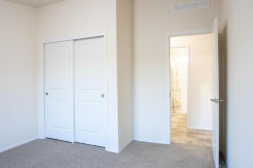 An empty room with white closets and carpet.